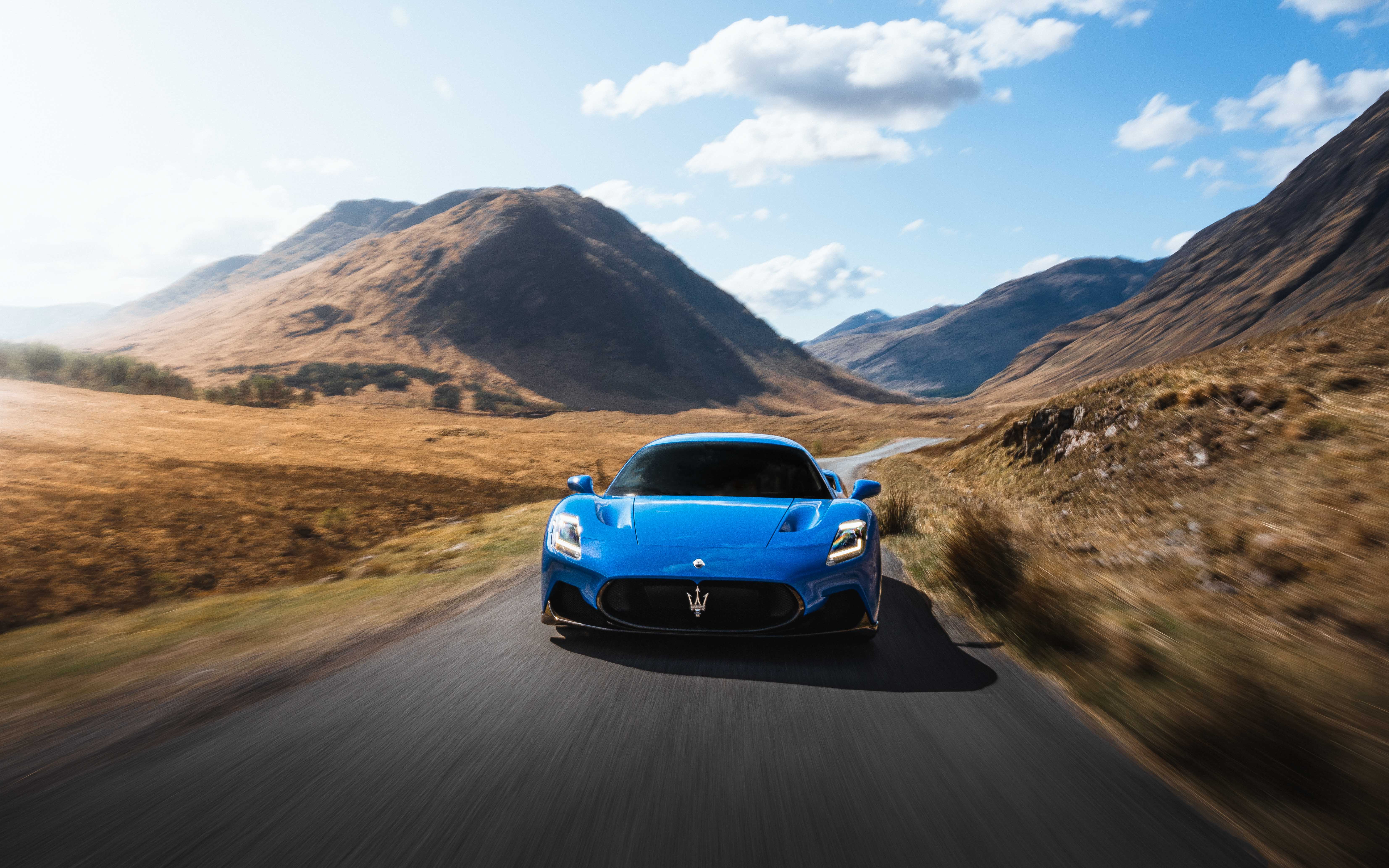 A blue Maserati driving with the Scottish Highlands in the background